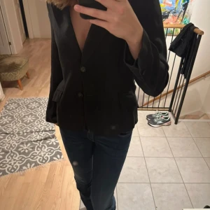 Svart kavaj från Mar Philippe - Snygg svart kavaj från Mar Philippe med klassisk design och knappar framtill. Perfekt för en stilren look. Passar bra till både jeans och mer formella byxor.