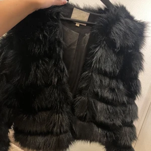 Svart pälsjacka - Snygg svart pälsjacka som ger en lyxig känsla. Perfekt för att hålla sig varm och stilren under kyliga dagar. Jackan har en fluffig textur och är lätt att matcha med olika outfits.