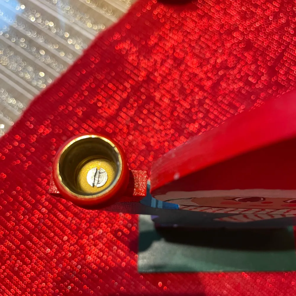 Charmig träfigur föreställande en tomte med röd luva och blå kläder. Tomten håller en ljushållare i handen, perfekt för juldekoration. Den har en vit och röd randig halsduk och står på en grön bas.. Asusteet.