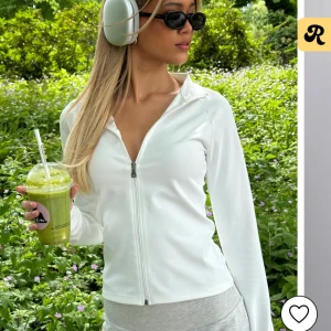 Nelly Vit zip-up hoodie - Snygg och stilren vit zip-up hoodie med dragkedja framtill. Perfekt för en avslappnad look eller träning. Den har en v-ringad design och långa ärmar.