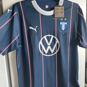 Blå Malmö FF fotbollströja från Puma - Snygg blå Malmö FF fotbollströja från Puma med vita och röda ränder. Tröjan har korta ärmar och ett stort VW-märke på framsidan. Perfekt för alla MFF-fans! Säljer pga fel storlek, gick ej att skicka tillbaka. Helt oanvänd med lappar kvar! Köpare står för frakt!