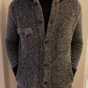 Grå kofta från Woolrich - Säljer en stilren grå kofta från Woolrich med knappar och en bröstficka. Varm och gjord av merino ull.