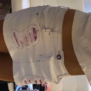 Vita lågmidjade kjol med paljettdetaljer - Snygga vita jeanskjol med lila paljettdetaljer och slitna effekter. De har en lågmidjad passform och lila sömmar som ger en unik look. Perfekta för en somrig stil! Storlek xs-s. Köpt från en vintagebutik utomlands
