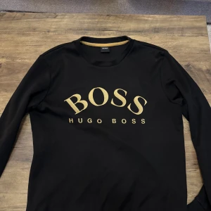 Svart långärmad tröja från Hugo Boss - Snygg svart långärmad tröja från Hugo Boss med guldigt BOSS-tryck på bröstet. Toppskick!