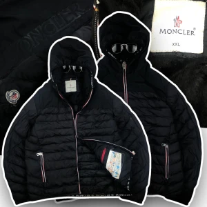 Svart dunjacka från Moncler - Snygg svart dunjacka från Moncler med huva och dragkedja. Jackan har Moncler-logga på bröstet och detaljer i rött, vitt och blått längs dragkedjorna. Insidan har en serietidningsdesign och en praktisk innerficka med röd dragkedja. Chest 46 cm. , sleeve length 60cm. , length form shoulder 63cm.