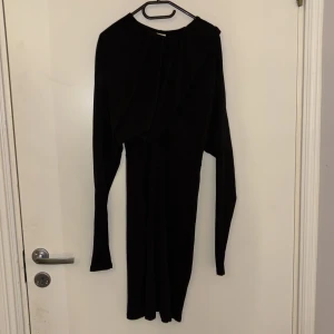 Svart långärmad klänning - Elegant svart klänning med lång ärm och asymmetrisk design. Perfekt för en stilren look.
