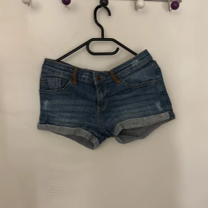 Blå jeansshorts - Snygga lågmidjade blå jeansshorts med uppvikta kanter och klassisk femficksdesign. Perfekta för en avslappnad sommarlook. De har en knapp och dragkedja framtill. Sitter bra i rumpan
