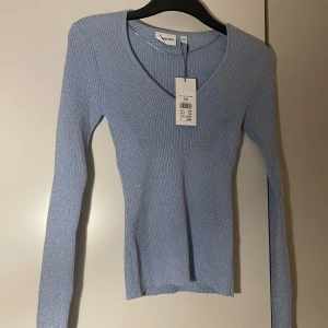 Blå ribbad tröja från Pieces - Snygg blå ribbad tröja från Kappahl med v-ringning och långa ärmar. Perfekt för en stilren look. Tröjan är i ett glittrigt material som ger en extra touch. Ny med taggar kvar.