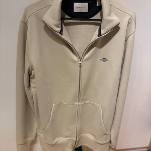 Beige ziptröja från GANT - Säljer en stilren beige ziptröja från GANT. Säljs i nytt skick för den har aldrig använts av mig. 