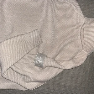 Beige stickad polotröja från Stone Island - Säljer en stilren beige stickad polotröja från Stone Island. Tröjan har en hög krage och ribbade muddar vid ärmslut och nederkant. Storlek XXL men passar XL