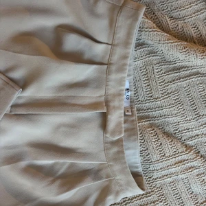 Beige kostymbyxor - Snygga beige kostymbyxor med hög midja och raka ben. Byxorna har diskreta fickor bak och en stilren design. Kroppade nedtill men passar mig i övrigt som är 180cm och vanligtvis bär S/M. 