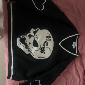 Svart tröja med dödskalle från Heaven Can Wait - Säljer en svart tröja från Heaven Can Wait med en stor vit dödskalle och texten 'HCW' på framsidan. Tröjan har vita detaljer vid ärmslut och nederkant samt en v-ringad hals. Äkta är alltså köpt på deras hemsida, kan visa orderbekräftelse om de önskas!!