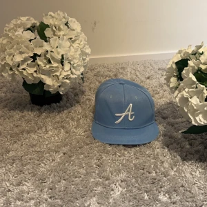 Ljusblå keps Mlb med ett A på - Snygg ljusblå keps med en vit broderad 'A' på framsidan och en färgglad patch med texten 'Los Angeles 1988' på sidan. Perfekt för en avslappnad stil. Pris kan diskuteras. TAR ENBART EMOT SWISH om inget bättre förslag. Köpt för 400kr