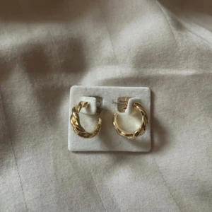 Guldiga örhängen - Snygga guldiga örhängen med en vriden design från glitter. Perfekta för att ge en elegant touch till din outfit. Passar både till vardag och speciella tillfällen. Aldrig använda.