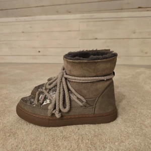 Grå  inukii boots med paljettdetaljer - Snygga grå inuikii boots med glittriga paljettdetaljer och tjocka snören. Insidan är fodrad för extra värme och komfort. Perfekta för kyligare dagar. Är använda 1 1/2 säsong.