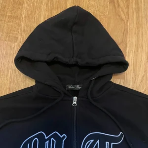 Svart hoodie tuttolente - Snygg svart hoodie med dragkedja och tryck på bröstet från Andrew Roger. Perfekt för en avslappnad stil med en skön huva och justerbara snören. Ett måste i garderoben för alla hoodie-älskare!