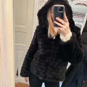 Svart pälsjacka med huva - Säljer en snygg svart pälsjacka med huva. Jackan har en dragkedja framtill och är perfekt för kyliga dagar! Ända defekten är ett hål på tyget på insidan men märks ej av💞tryck gärna på köp nu! 