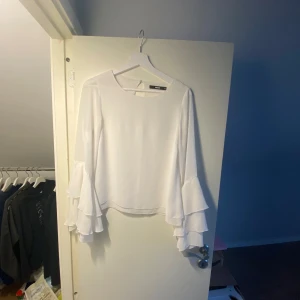 Vit blus med volangärmar - Säljer en stilren vit blus från BikBok med långa volangärmar och en liten öppning i ryggen.
