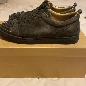  Christian Louboutin skor - Snygga svarta sneakers i mocka från Christian Louboutin med coola nitar på tån och klassisk röd sula. Perfekta för att ge din stil en edgy touch. Priset är inte hugget i sten. 2 spikar saknas på ena skon inget som syns egentligen. De är äkta. Skulle kunna byta mot något annat par skor 