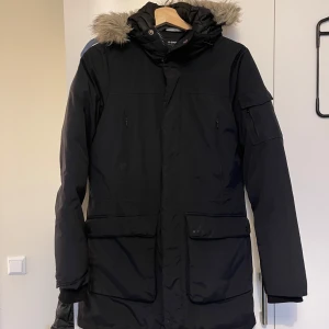 Svart parkajacka med pälskantad huva - Säljer en svart parkajacka från Everest med pälskantad huva. Jackan har långa ärmar och flera praktiska fickor. Perfekt för kalla dagar med sin varma vaddering och stilrena design.