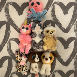 Samling av Ty Beanie Boos nyckelringar - Säljer en samling av sju Ty Beanie Boos nyckelringar. Inkluderar en rosa bläckfisk, en rosa enhörning, en grå katt, en beige sengångare, en leopard, en brun och vit hund samt en gul och vit hund. Perfekta som söta accessoarer eller samlarobjekt!