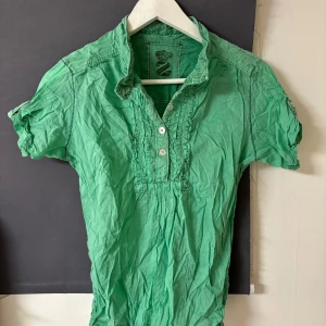 Grön kortärmad henley - Säljer en grön kortärmad henley från Brand i storlek S. Skjortan har knappar framtill och fina detaljer vid kragen. Perfekt för en avslappnad stil.