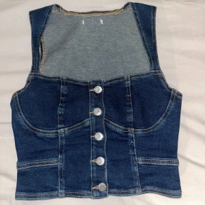 Jeansväst med knappar - Snygg jeanstopp med knappar framtill. Västen har en klassisk blå denimfärg och är perfekt för en trendig look. Den har en figurnära passform och stilrena sömmar som ger en cool touch storlek s men passar xs