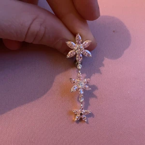 Glittriga Navelpersing med blommotiv - Snygga och eleganta Navelpersing med glittrande stenar i form av blommor. Perfekta för att ge en extra touch av glamour till din outfit. De har en hängande design med flera blommor i rad.