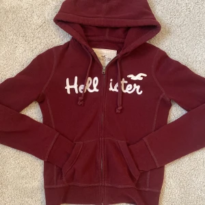 Vinröd hoodie från Hollister - Säljer en snygg vinröd hoodie från Hollister med dragkedja och huva. Storlek XS🤍 Pris kan diskuteras.