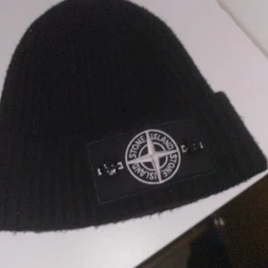 Svart ribbad mössa från Stone Island - Snygg svart ribbad mössa från Stone Island med det ikoniska märket framtill. Perfekt för att hålla värmen under kyliga dagar.