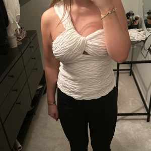 Vit oneshoulder topp - Snygg vit oneshoulder topp med knytning framtill. Den har en unik textur och är perfekt för en kväll ute. Passar bra med både jeans och kjol.