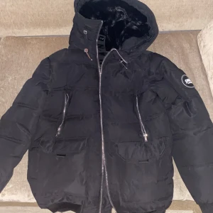 Svart pufferjacka från Supply & Demand - Snygg svart pufferjacka från Supply & Demand med dragkedja och huva. Jackan har en mjuk insida och flera praktiska fickor med dragkedjor. Perfekt för kyliga dagar. Helt oanvänd och i nytt skick. Päls ingår i köpet. Köpt för 1550!