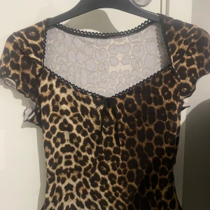 Leopardmönstrad topp med spetsdetaljer - Trendig leopardmönstrad topp med korta ärmar och spetskant vid halsringningen. Toppen har en söt knytning framtill och är perfekt för en djärv look.