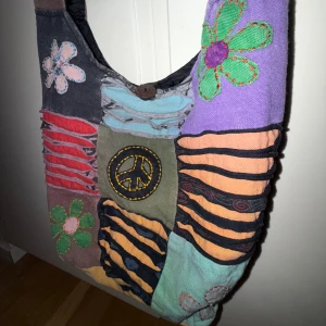 Färgglad hippie axelväska med patchwork☮️ - Unik axelväska i patchwork-stil med färgglada ränder och applikationer av blommor och en fredssymbol. Väskan har en knappstängning och är perfekt för en bohemisk look. Är i bra skick! Tar bara emot Swish! Så köp inte direkt och fråga gärna mig om ni undrar något! Skickar postbevis! Frakt: 65kr 