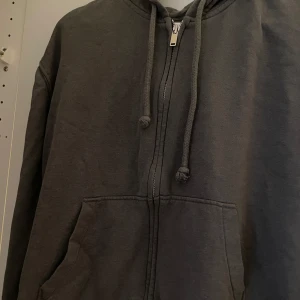Mörkgrå kofta - Säljer en mörkgrå kofta från H&M med dragkedja. Perfekt för en avslappnad stil med praktiska fickor framtill. Passar bra till kyligare dagar.