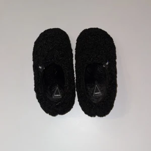Svarta tofflor från Verbenas - Mysiga svarta tofflor från Verbenas med en fluffig yta. Perfekta för att hålla fötterna varma och bekväma inomhus. De har en enkel design utan snörning eller andra detaljer. Helt oanvända