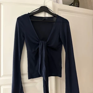 Mörkblå topp från Gina Tricot - Säljer en snygg mörkblå topp från Gina Tricot med långa ärmar och knytning framtill. Perfekt för en stilren look. Toppen är i en mjuk och bekväm kvalitet.