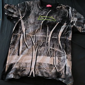 Camouflage T-shirt från Diesel - Säljer en cool T-shirt från Diesel med ett unikt camouflage-mönster i svart och beige. T-shirten har korta ärmar och ett grönt Diesel-tryck på bröstet och ryggen. Perfekt för en avslappnad stil.
