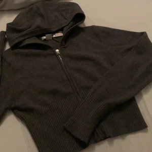 Mörkgrå tröja från Gina Tricot - Säljer en mörkgrå tröja från Gina Tricot med dragkedja framtill. Tröjan har en ribbad nederkant vilket ger en snygg och bekväm passform. Använd 1 gång, köpt för 250kr