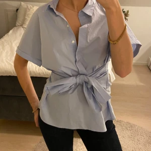 Ljusblå blus från InWear - Säljer en stilren ljusblå blus från InWear med korta ärmar och knytning i midjan. Blusen har en klassisk krage och knappar framtill. Perfekt för en chic och avslappnad look. 💙