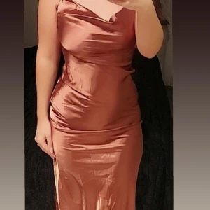 Brun långklänning i satin - Elegant brun ungefär knälång klänning i satin med smala axelband och en vacker drapering framtill. Perfekt för en stilfull kväll.