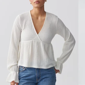 Vit blus med v-ringning - Säljer en stilren vit blus med v-ringning och långa ärmar. Blusen har en omlott-design och är tillverkad i ett lätt och luftigt material. Perfekt för en chic och avslappnad look.