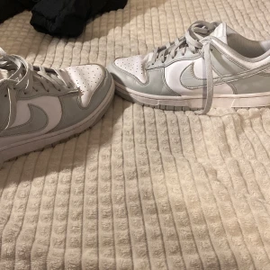 Nike Dunk grey frog - Snygga Nike Dunk i vitt och grått. Skorna har en klassisk design med snörning och den ikoniska Nike-loggan på sidan. Perfekta för en stilren look. De är använda därav priset. Lådan medföljer
