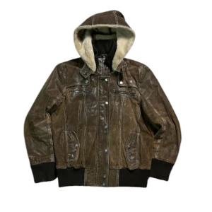 Brun skinnjacka med huva från JCC - Snygg brun skinnjacka från JCC med avtagbar huva fodrad i mjuk pälsimitation. Jackan har dragkedja och knappar framtill samt ribbade muddar vid ärmslut och nederkant. Perfekt för kyligare dagar! Kom gärna med frågor! Måtten är 63 cm på längden och axel bredden är 41,5 cm.