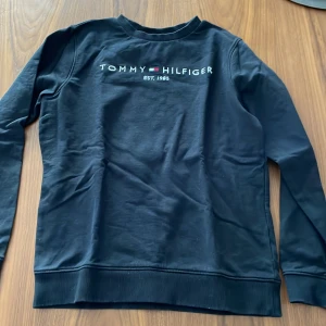 Svart tröja från Tommy Hilfiger - Snygg svart tröja från Tommy Hilfiger med broderad logga på framsidan. Bra skick. Storlek 164 men skulle säga att det är som XS