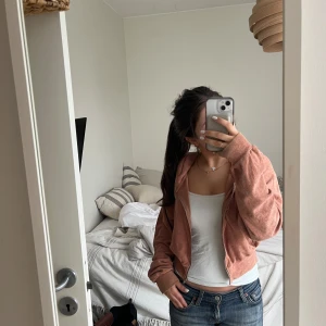 Rosa croppad hoodie - Säljer en snygg rosa croppad hoodie med dragkedja framtill. Den är från Bikbok i storlek xs Den har en avslappnad passform och långa ärmar, perfekt för en chill look. Hoodien är gjord i ett mjukt material som känns skönt mot huden.