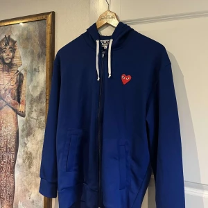 Blå hoodie med hjärtdetalj - Snygg blå hoodie från Comme des Garçons Play med dragkedja. Storlek XL men passar M/L