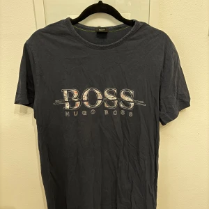Mörkblå t-shirt från Hugo Boss - Snygg mörkblå t-shirt från Hugo Boss med stort BOSS-tryck på framsidan. T-shirten är kortärmad och har en klassisk rund halsringning. 