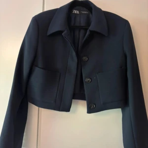 Svart croppad kavaj från Zara - Snygg svart croppad kavaj från Zara med knappar framtill. Perfekt för en stilren look. Långärmad design med klassisk krage.