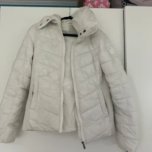 Vit pufferjacka från stadium - Säljer en snygg vit pufferjacka från stadium. Jackan har en dragkedja framtill och en hög krage för extra värme. Det är storlek S/36